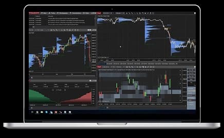 MacBook Pro displaying a futures trading platform interface with live market charts and trading tools on the screen.
